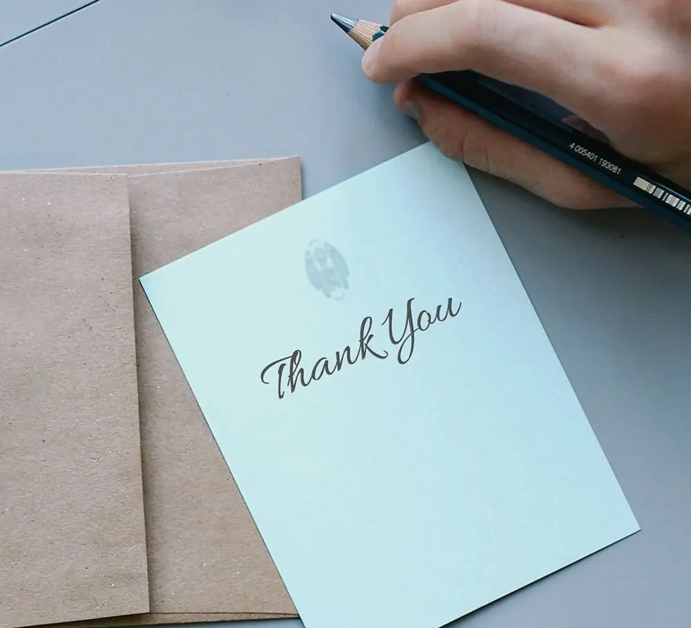 「Thank You」と書かれたカードと封筒、ペンを持つ手